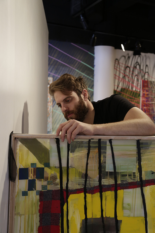 A working shot of an impossibly handsome and rugged male artist, approximately 29 years old, with in progress paintings and installations.